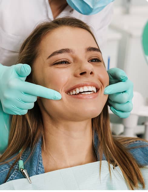 MI Smile Family Dental | Dental patient smiling as a dentist gently checks her teeth during an exam