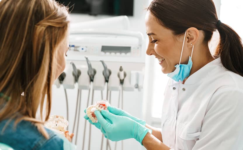 MI Smile Family Dental | Dentist smiling while showing a young patient a dental model during a consultation